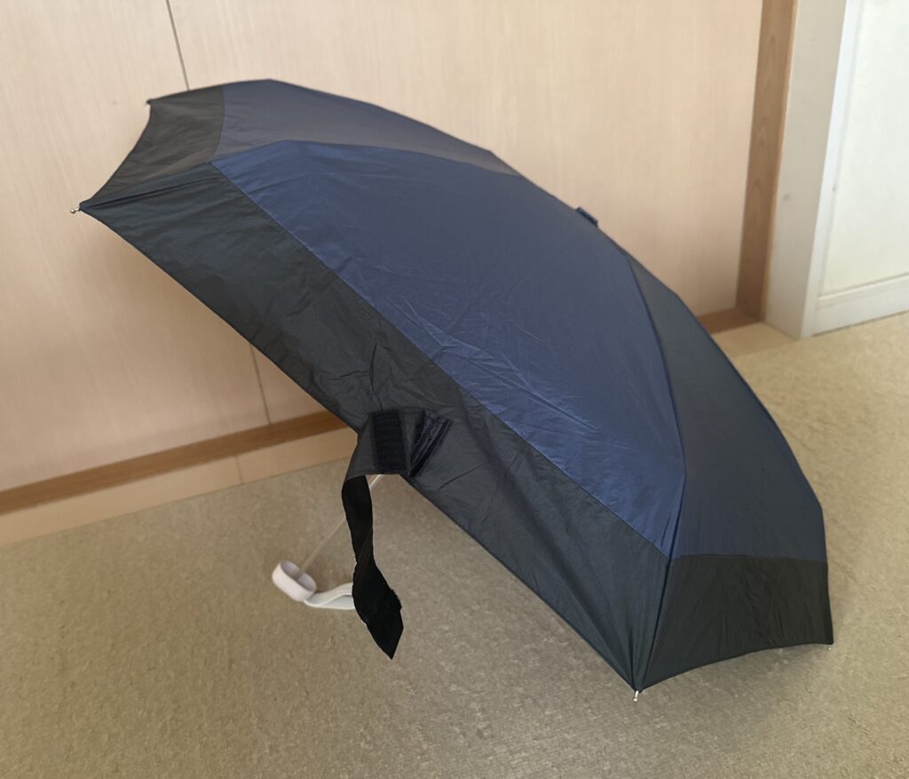 Wpc.の折りたたみ日傘を横から斜めに撮影。使用時のサイズ感と首元までしっかりカバーする様子がわかる。